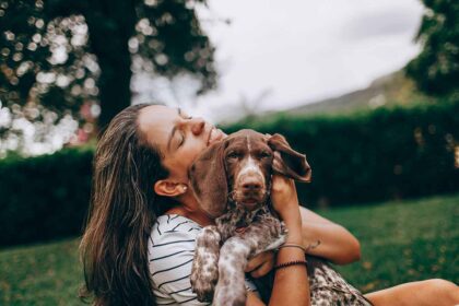 a girls standing with a dog on her lap in the field